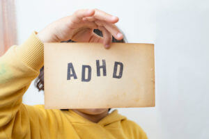 A child's hand holds a vintage paper page displaying the abbreviation ADHD.